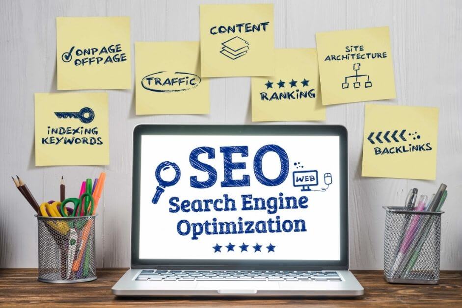 SEO v. Social Media - SEO - Search Engine Optimization on laptop with post it notes around that say indexing keywords, on page, off page, traffic, ranking, site architecture, and backlinks